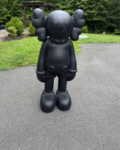 A lifesize 3D printed black KAWS-style figure, about 4 ft tall, standing in a driveway